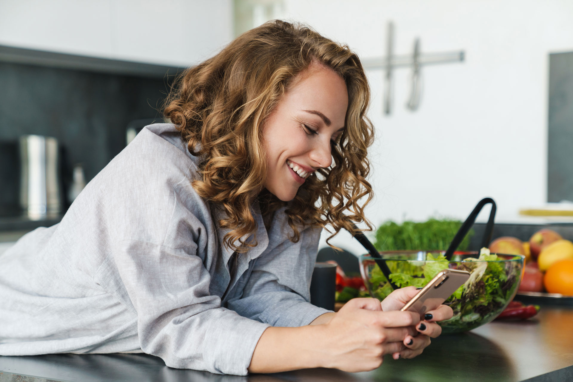 smiling-young-woman-using-smartphone-in-kitchen-3K5MASW.jpg